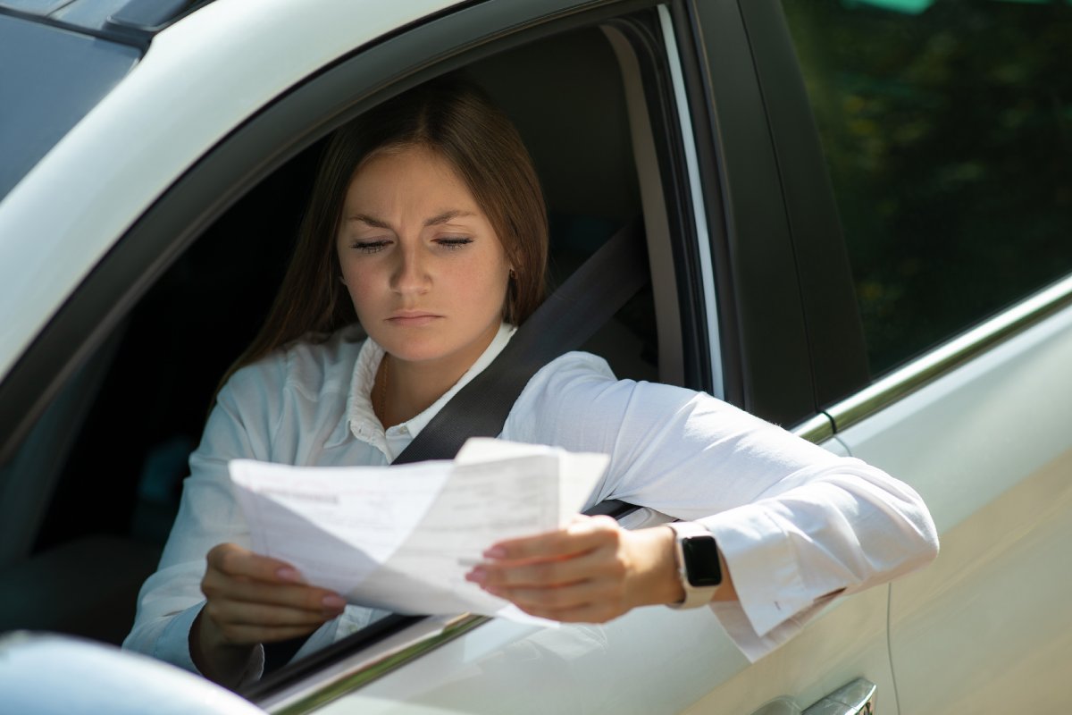 Multa por ultrapassar faixa continua - Na imagem: mulher sentada no banco do motorista analisando uma multa