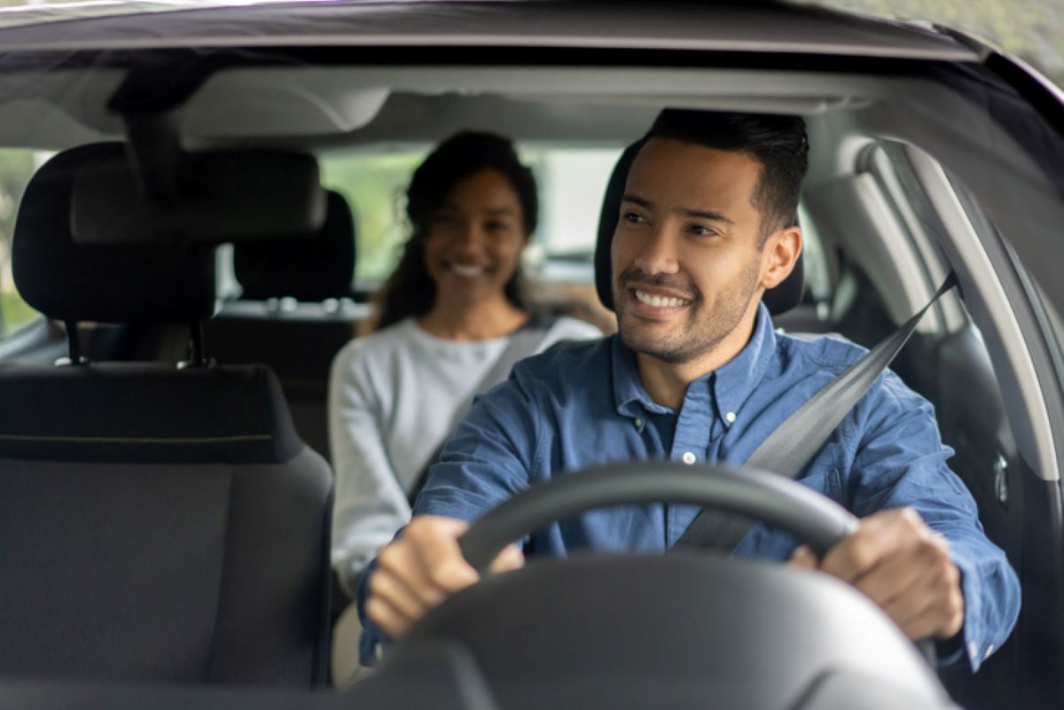 Duas pessoas em um carro sendo uma pessoa dirigindo e a outra passageira no banco de trás.