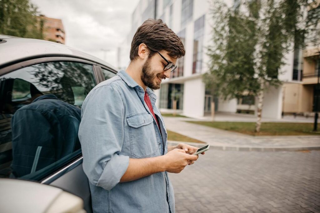 Seguro auto Youse é bom - Na Imagem uma pessoa enconstado em um carro mexe no celular